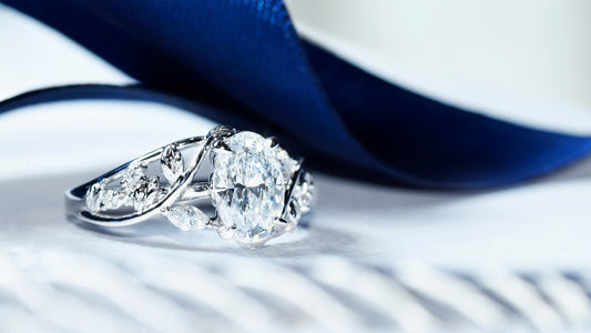 Custom white gold engagement ring with open line curved band, leaf-shaped details, and oval diamond in four-prong setting