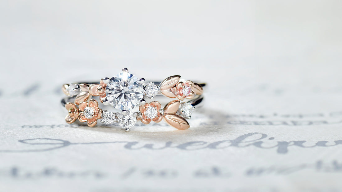 Custom white gold engagement ring with rose gold floral and leaf design, pavé diamonds, and matching stacking band