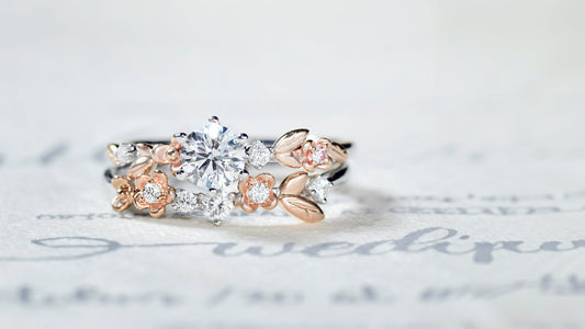 Custom white gold engagement ring with rose gold floral and leaf design, pavé diamonds, and matching stacking band