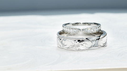 Custom white gold wedding bands featuring engraved designs, milgrain edges, pavé diamonds, and princess-cut diamond accent on men’s ring