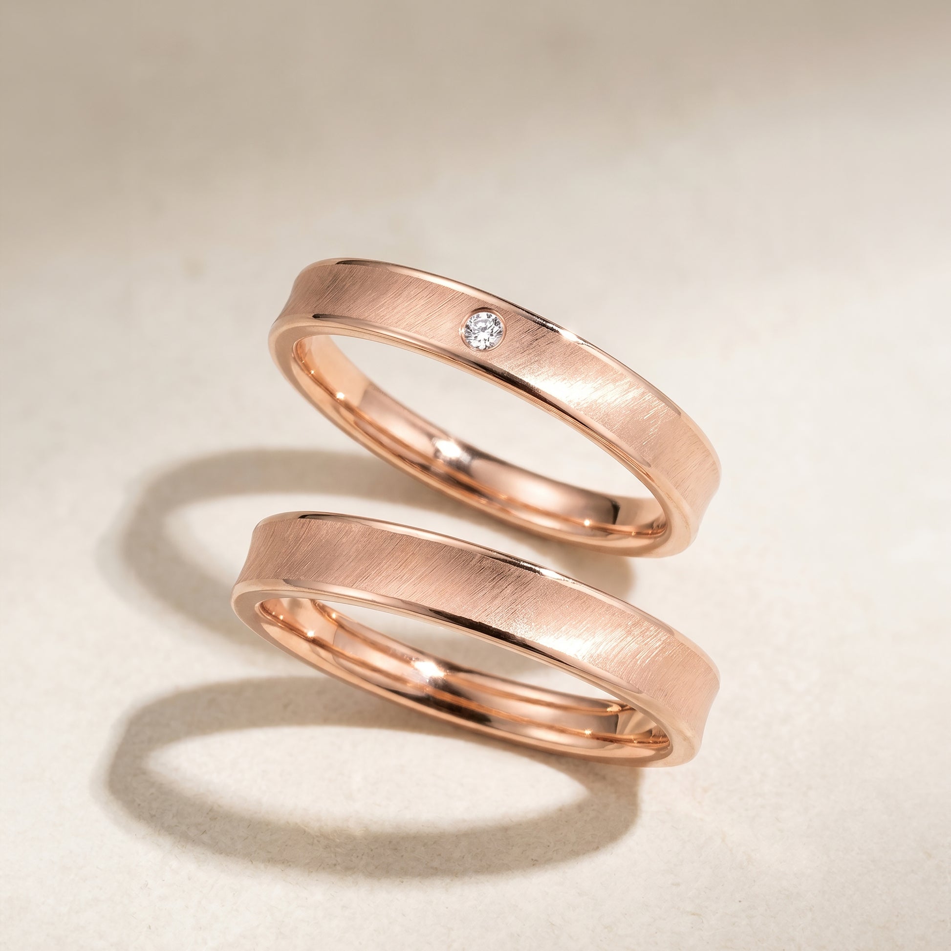 A set of rose gold wedding band on a beige background. Lady's band with diamond